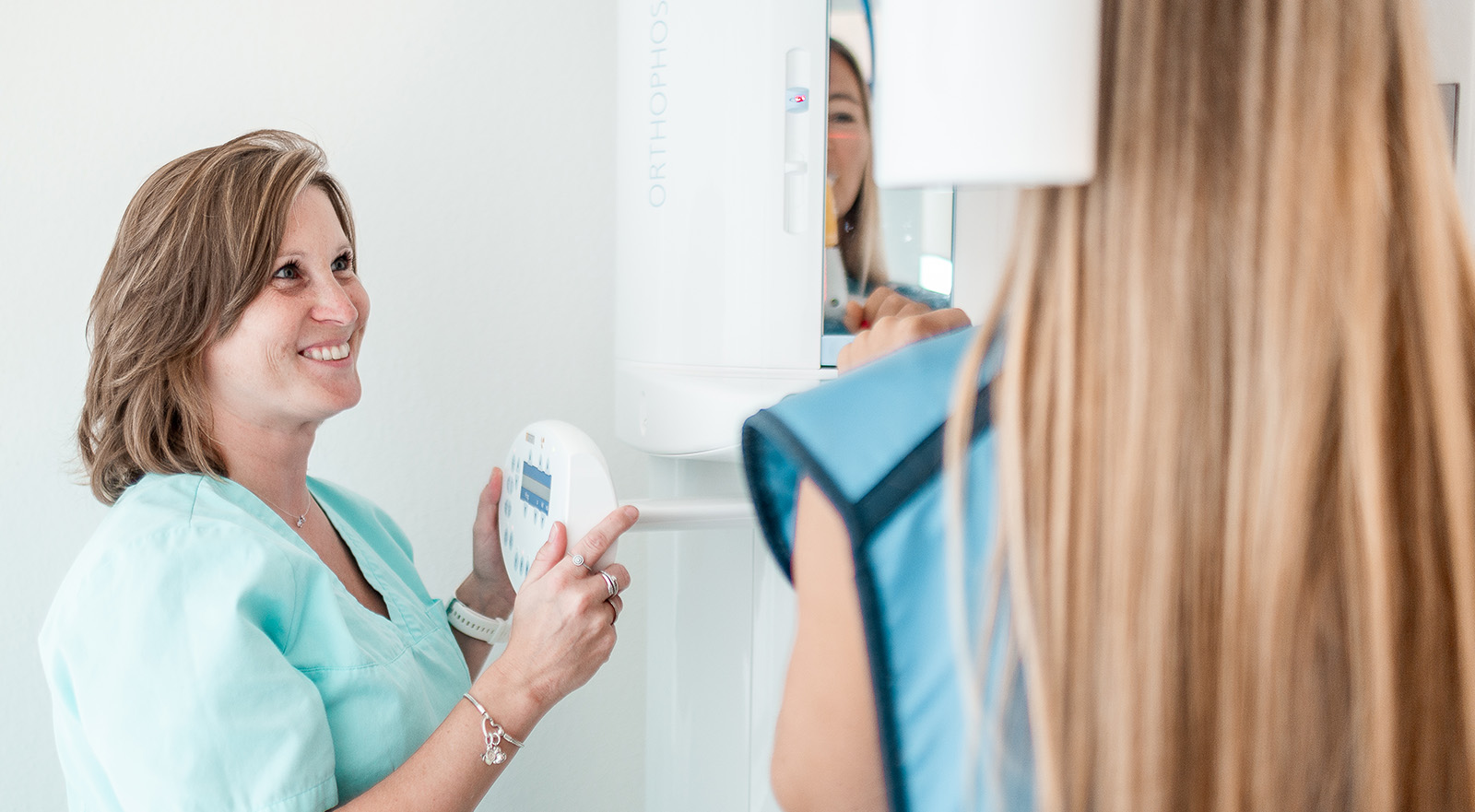 ZFA lächelt Patientin in der Zahnarztpraxis Am weißen Turm in Darmstadt an. Patienten steht mit dem Rücken zum Betrachter und hat ihren Kopf in einem Röntgengerät fixiert, hier entsteht ein DVT zur besseren Planung der Zahnimplantate in Darmstadt.